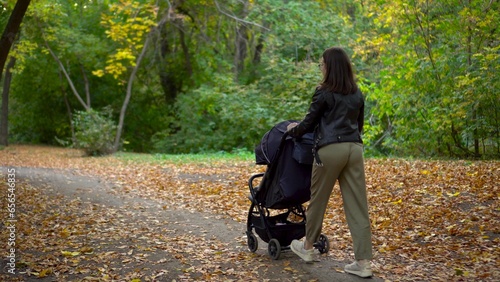 A young mother walks through the forest with a sleeping child in a stroller. A woman with glasses walks in an autumn park. © Vital9c