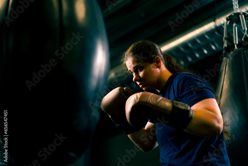 a girl boxer in gloves works out the power of punches on a punching bag in the gym trains hard before the fight
