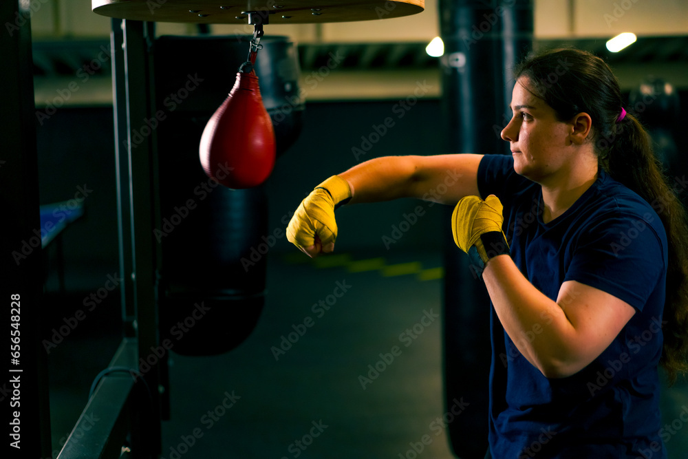 a girl boxer in gloves works out the strength of blows and coordination on a small punching bag in the gym trains diligently before the fight