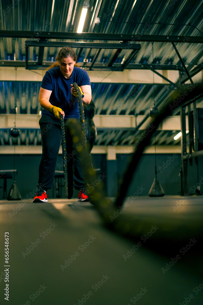 Fototapeta premium concentrated female athlete doing exercises with ropes in gym training muscles sport concept