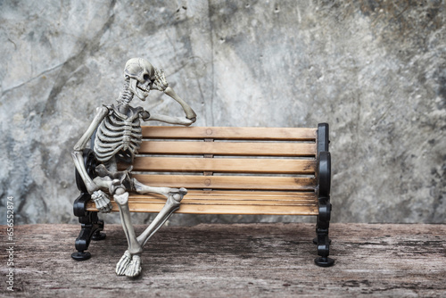 Skeleton ghost sits sleepily on a an old bench with dark background gothic or loft style. photo