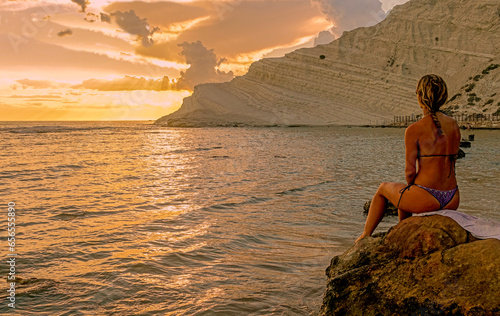 Donna seduta su una roccia che osserva il tramonto sul mare 9866 photo