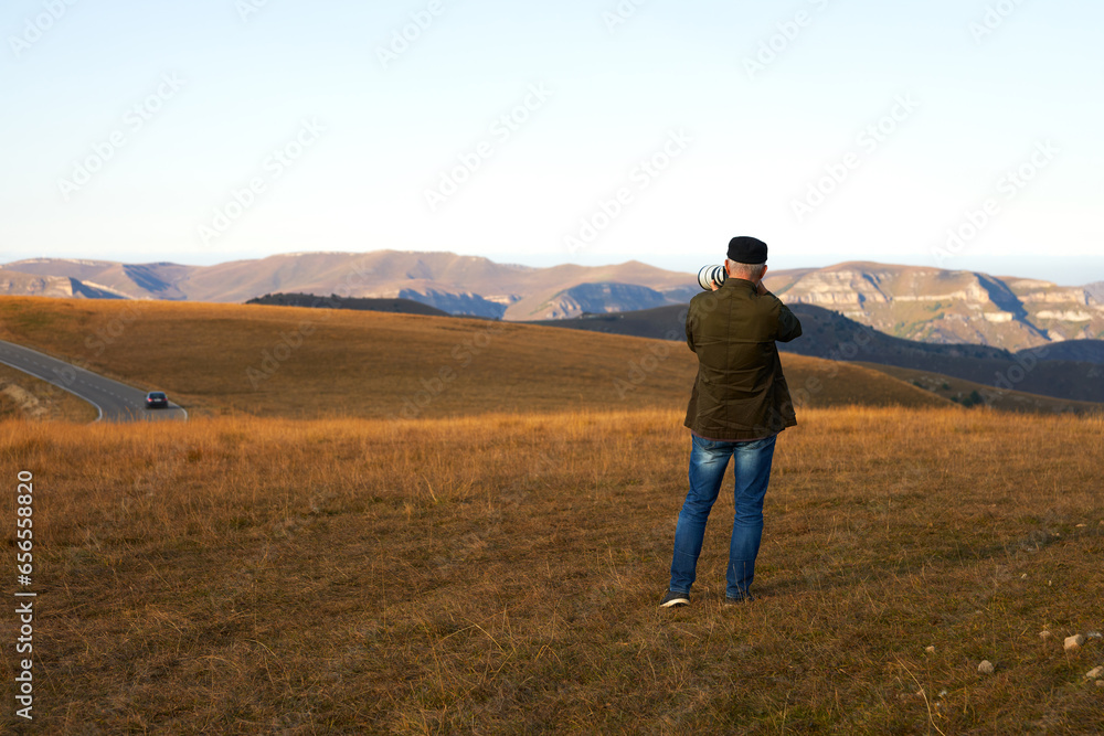 An adult male photographing a mountain landscape with a long lens. Copy space.