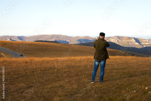 An adult male photographing a mountain landscape with a long lens. Copy space. © ROMAN DZIUBALO