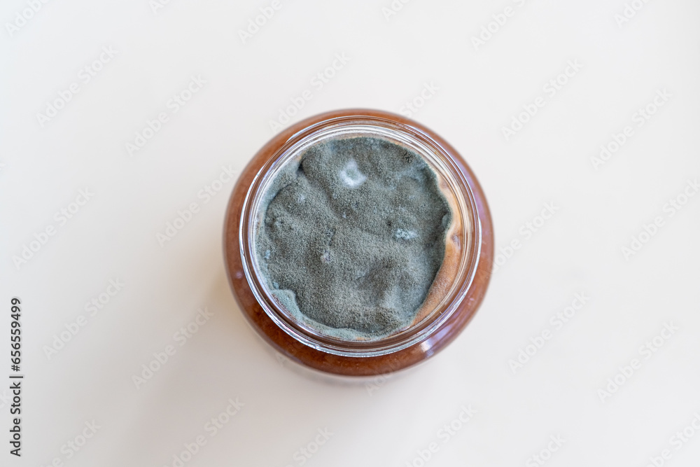 Open jar with sweet jam and mold on a white background. Mold in a jar of raspberry jam. Hazardous to health. Open jar with sweet jam and mold on a white background. Mold in a jar of raspberry jam. Hazardous to health.