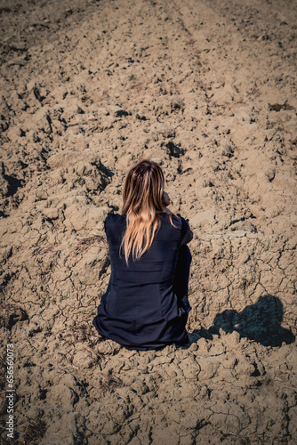 Thoughtful woman sitting on the ground in a dry field