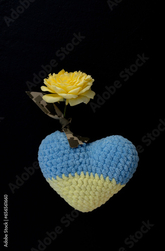 yellow-blue Ukrainian knitted heart, yellow rose tied with a camouflage ribbon on a black background. patriotism, tragic military actions in Ukraine, mourning for fallen soldiers. Stop the war