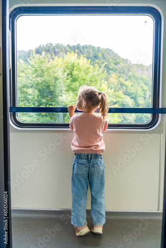 Little girl looking out train window outside, while it moving. Traveling by railway in Europe