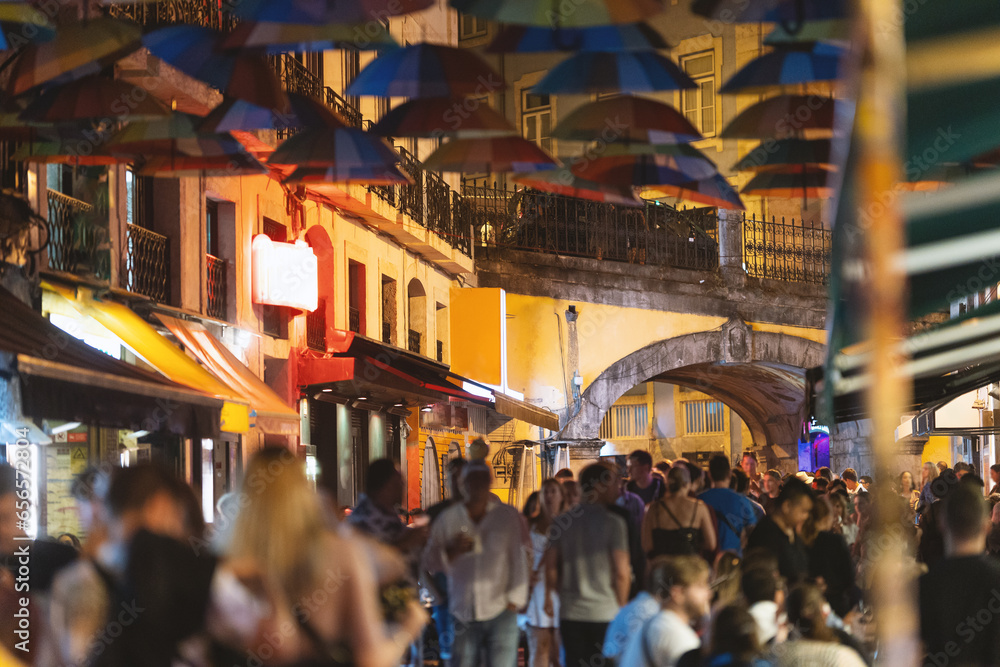 Colorful umbrellas over the street of Portugal - people walk around the city in the evening near a cafe