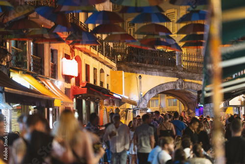 Colorful umbrellas over the street of Portugal - people walk around the city in the evening near a cafe