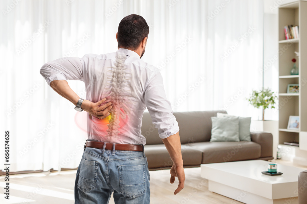 Rear view shot of a man with painful back in a living room Rear view shot of a man with painful back in a living room