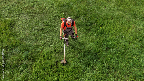 Aerial view of worker in protective clothing cutting grass with brush cutter photo