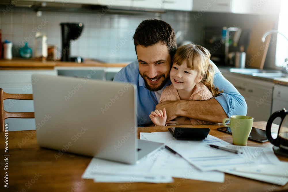 Young father embracing his daughter while paying bills in the kitchen Young father embracing his daughter while paying bills in the kitchen