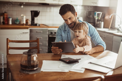 Young father using the tablet with his daughter in the kitchen