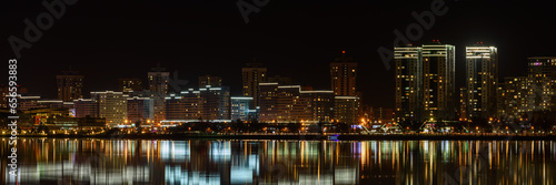 modern night big city with tall buildings glows beautifully with electric lights and is reflected on the water of the lake. Coastal Avenue. widescreen panoramic cityscape in 15x3 format. Minsk © gluuker