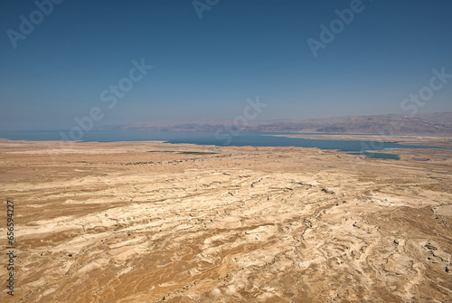 From Masada, Israel, gaze eastward to a breathtaking vista. The vast desert sprawls beneath, and the shimmering Dead Sea, nature's mirror, glimmers in the distance, creating a mesmerizing panorama.