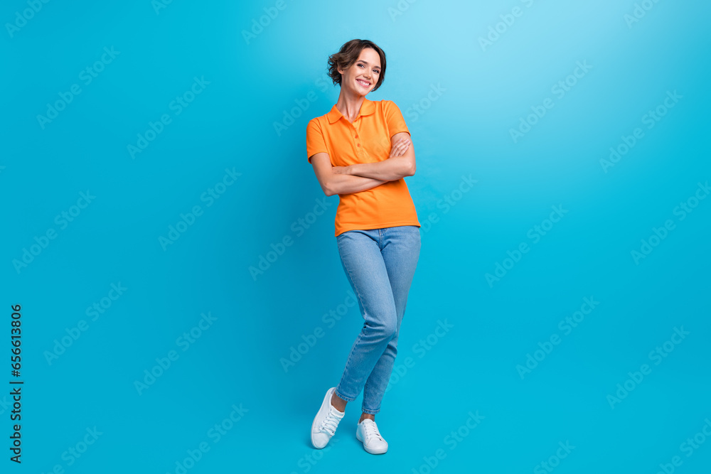 Full size photo of optimistic cute gorgeous girl dressed stylish polo jeans pants holding arms folded isolated on blue color background Full size photo of optimistic cute gorgeous girl dressed stylish polo jeans pants holding arms folded isolated on blue color background
