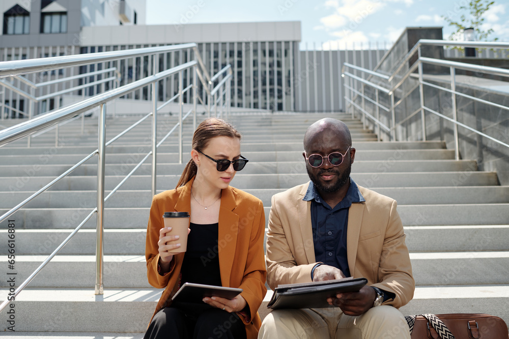 Young African American male employee in formalwear pointing at document during presentation of financial data to female colleague