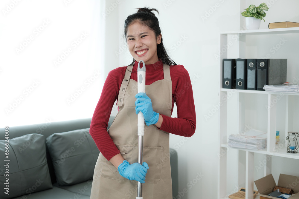 Happy young woman cleaning her home, singing at mop like at microphone and having fun Happy young woman cleaning her home, singing at mop like at microphone and having fun