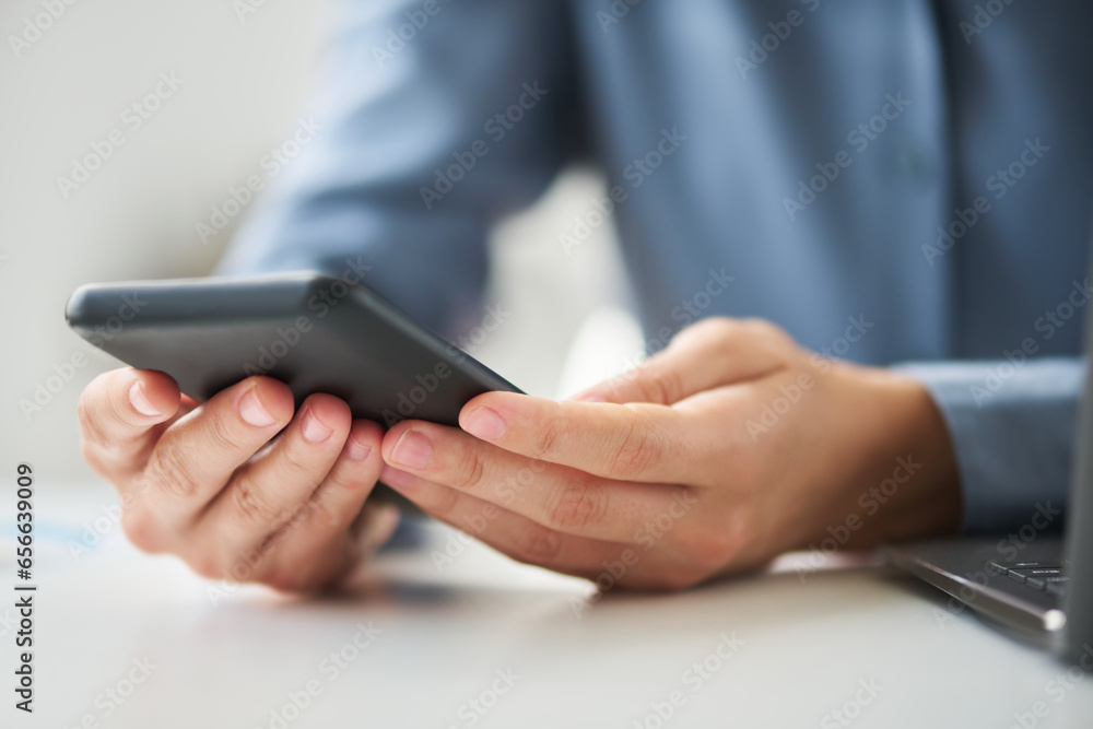 Close-up of hands of young modern white collar worker with mobile phone sitting by desk in front of camera in office and texting Close-up of hands of young modern white collar worker with mobile phone sitting by desk in front of camera in office and texting