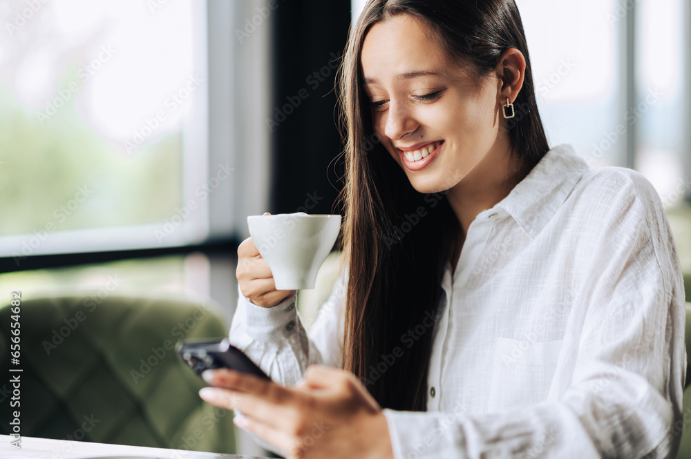 Young happy woman scrolling on the phone while sitting in a coffee shop Young happy woman scrolling on the phone while sitting in a coffee shop