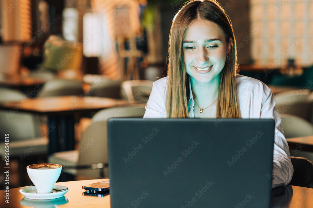Portrait of a cheerful freelancer sitting in a cafe and typing on a laptop while smiling Portrait of a cheerful freelancer sitting in a cafe and typing on a laptop while smiling
