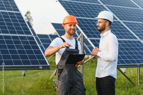 Businessman and worker near solar energy batteries. Business client showing photovoltaic detail to foreman. Two men making deal. © Serhii