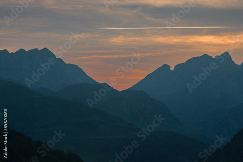 sunrise or sunset in the silhouette of the mountains with redish and orange tones with the line of a plane flying over them