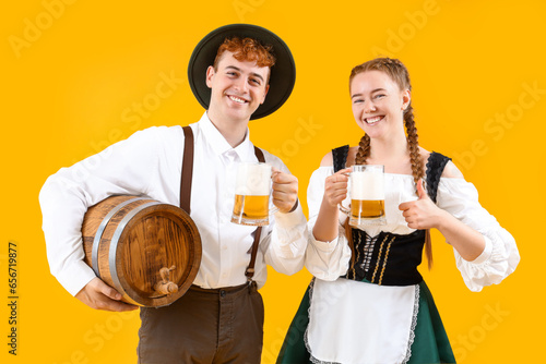 Young couple in traditional German clothes with beer on yellow background