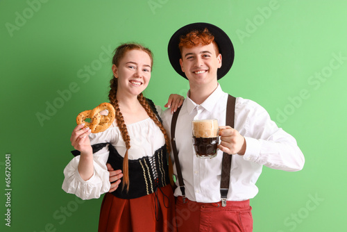 Young couple in traditional German clothes with beer and pretzel on green background