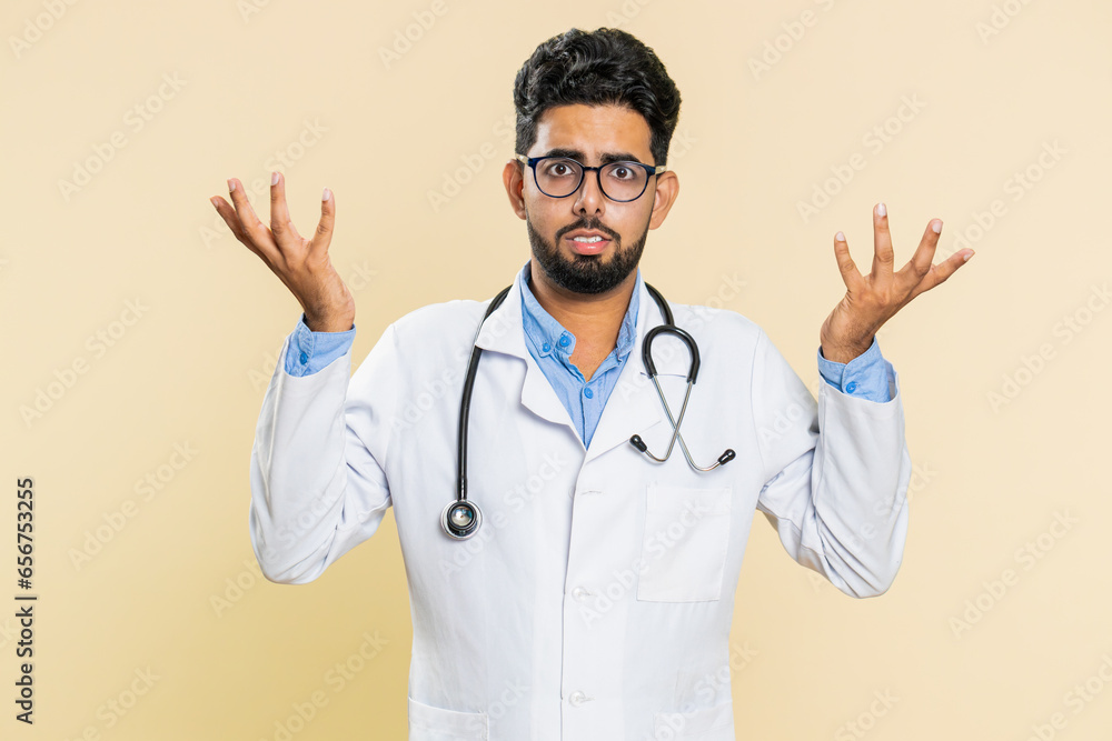 What. Why. Confused Indian doctor cardiologist man raising hands in indignant expression asking reason of failure, demonstrating disbelief irritation by troubles. Apothecary guy on beige background What. Why. Confused Indian doctor cardiologist man raising hands in indignant expression asking reason of failure, demonstrating disbelief irritation by troubles. Apothecary guy on beige background