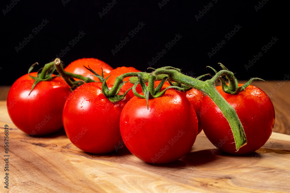 Fresh ripe tomato on a vine in plastic tray on wooden table surface, dark background. Organic product. Food supply chain industry. High quality vegetable. Fresh ripe tomato on a vine in plastic tray on wooden table surface, dark background. Organic product. Food supply chain industry. High quality vegetable.