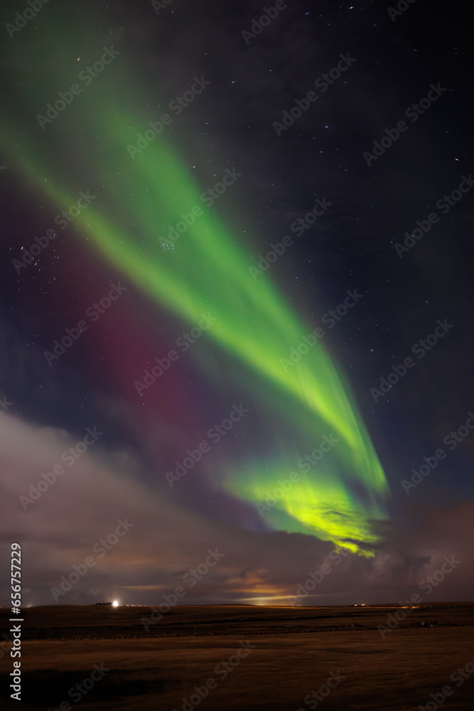 During wintertime, famous northern lights spotted over hills covered with snow. Icelandic magical aurora borealis create incredible show that brighten up cold night sky with stars.
