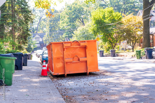 Photography A roll-off construction dumpster parked on a residential street with traffic cones on a shady street in an older neighourhood