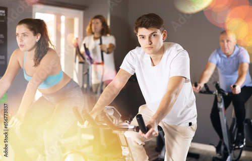 Motivated young guy leading healthy active lifestyle doing cardio workout on exercise bike in gym photo