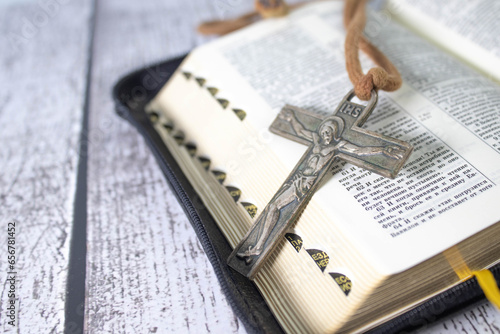 Wooden cross on top of an open bible and wood table. Copy space.