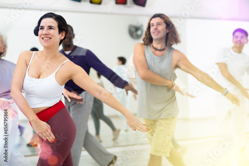 Happy young Latina enjoying active dancing during group training in dance studio..