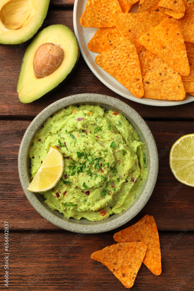 Bowl of delicious guacamole, lime and nachos chips on wooden table, flat lay Bowl of delicious guacamole, lime and nachos chips on wooden table, flat lay