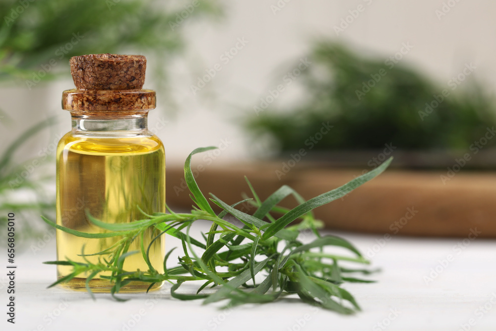 Bottle of essential oil and fresh tarragon leaves on white wooden table. Space for text Bottle of essential oil and fresh tarragon leaves on white wooden table. Space for text