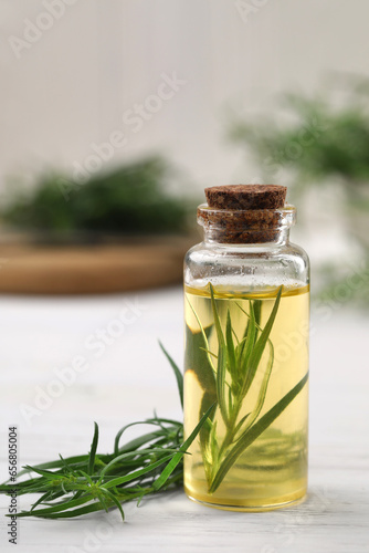 Foto Bottle of essential oil and fresh tarragon leaves on white wooden table