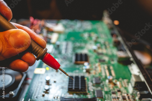 Hand holding a multimeter test lead: examining the hardware, circuits and components of a computer board