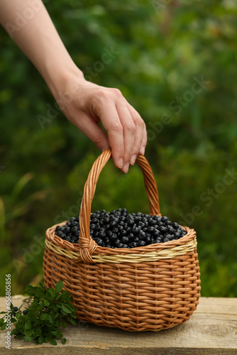 Woman taking wicker basket with bilberries at wooden table outdoors, closeup