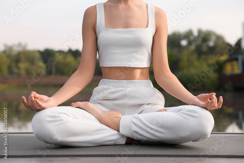Woman practicing Padmasana on yoga mat outdoors, closeup. Lotus pose