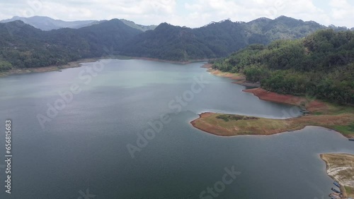 Aerial drone view of the reservoir dam with a background of clouds, hills and green trees photo