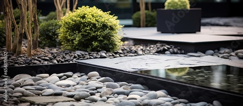 Stone elements adorn a modern houses yard and garden featuring a small square pond with gravel and water along with rocks