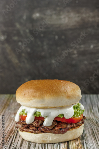 Churrasco italian sandwich popular in chile, round bread, beef, tomato and palta, mayonnaise, on wooden table, vertical, copy space. Typical Chilean food concept