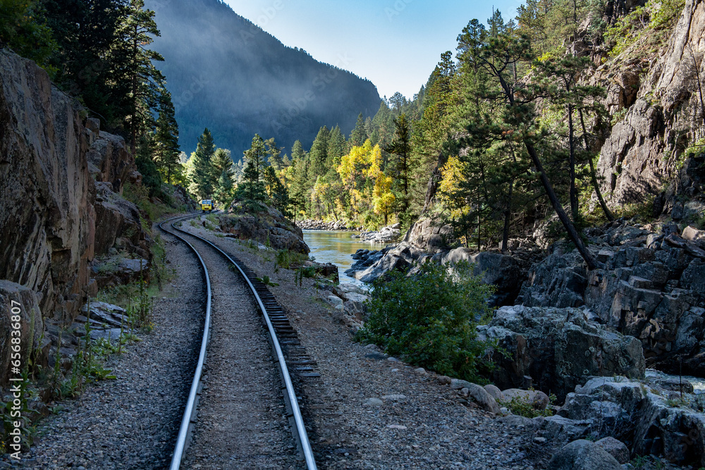 landscape view of railroad tracks traveling through the Colorado mountains on an autumn day along the river as aspen trees glow yellow in the sunlight