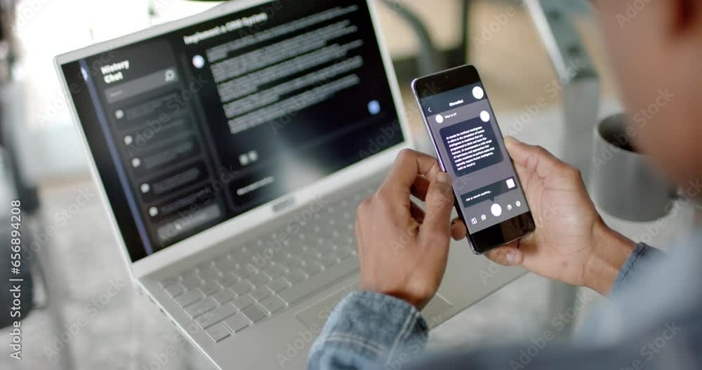 African american businessman using smartphone and laptop with ai chatbot at home, slow motion