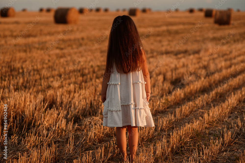 little girl in white saafans spend time in a field of cut wheat among the bales at sunset little girl in white saafans spend time in a field of cut wheat among the bales at sunset