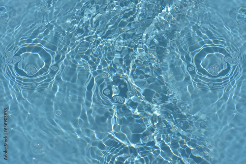 Defocus blurred transparent blue colored clear calm water surface texture with splashes reflection. Trendy abstract nature background. Water waves in sunlight with copy space. Blue watercolor shine.